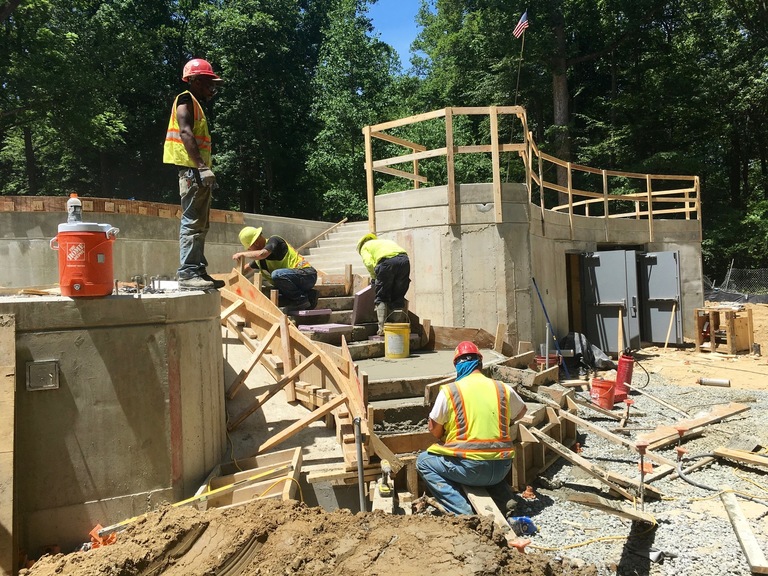 Workers pouring concrete for the stairs at the back of the Chrysalis. (Click for a higher-resolution version.)  The worker to the left is standing on one of the reinforced concrete piers of the Chrysalis; to the right are the doors leading into the two basement rooms of the subfloor. Image © 2016 Inner Arbor Trust; used with permission.