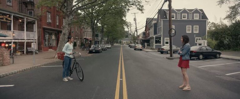 In the next to final scene of The Half of It, Ellie (left) and Aster (right) stand of opposite sides of the street and face each other, separated by a painted double yellow line.