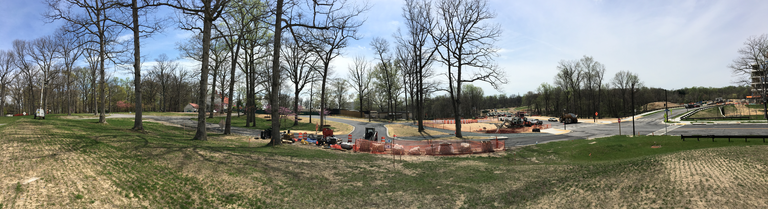 Panoramic view of the areas of Merriweather Park at Symphony Woods addressed by phase 7 of SDP-14-073 and by SDP-16-018. (Click for a higher-resolution version.) The view is south-southeast toward Merriweather Post Pavilion, with the future Free To Be Drive in the foreground extending from the extreme left to the stop sign at the intersection with the future Merriweather Drive, the lower end of the drop-off loop to Merriweather Park and the new pavilion box office in the center (behind the small piece of construction equipment), and the new parking lot with handicap spaces in the center right (behind the row of barrels). Image © 2017 Frank Hecker; available under the terms of the Creative Commons Attribution 4.0 International License.